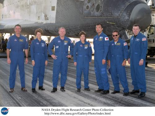 The seven members of the Space Shuttle mission STS-114 stand in front of the Space Shuttle Discovery for a group photo in their blue flight gear.