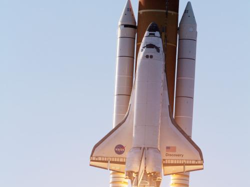 Space Shuttle Discovery, a plane-like object used in space which is attached to three large rockets, is soaring in the atmosphere towards space.