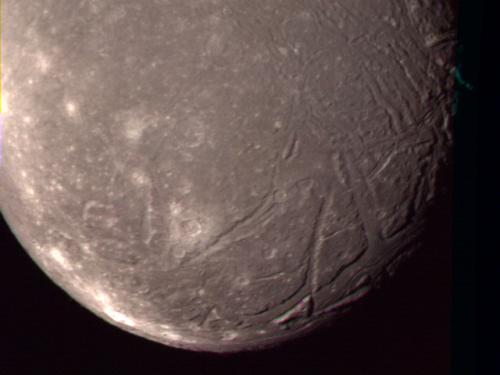 A close-up view of Ariel, a moon of Uranus, and some of its terrain with large craters creating lines