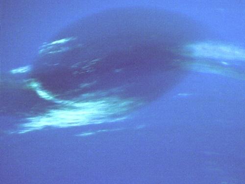 A view of Neptune's Great Dark Spot, a darker blue area of Neptune with light blue wisps near the bottom and the sides.