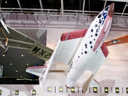 A red, white, and blue rocket-shaped spacecraft with foldable wings displayed inside the National Air and Space Museum.