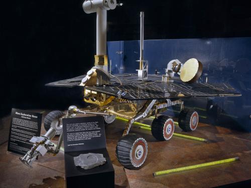 Large spacecraft model with six sturdy wheels, a flat platform covered with solar panels, and a vertical boom with camera on top.