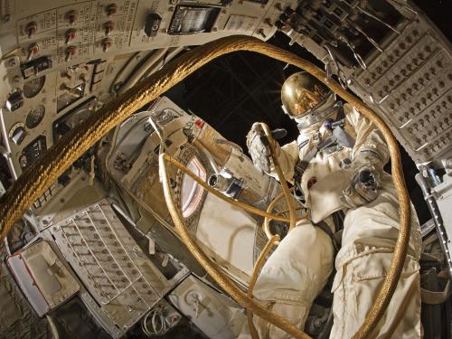 View from inside Gemini spacecraft with spacesuit emerging from the open door to visually simulate the first U.S. spacewalk.