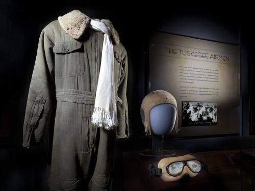 Flight suit, scarf, helmet, and goggles displayed next to Tuskegee Airmen graphic