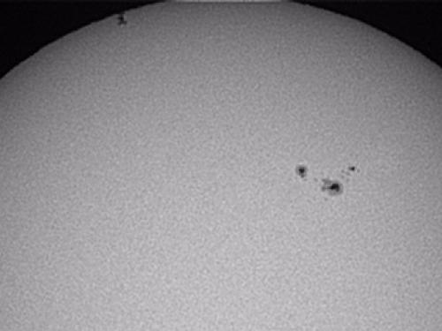 A partial view of the Sun as the International Space Station, a set of dots on the upper left side of the photo, transits the Sun.