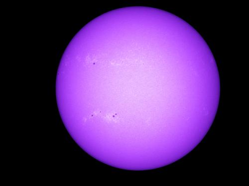 Disk view of the Sun with visible sunspots on the left side of the visible surface.