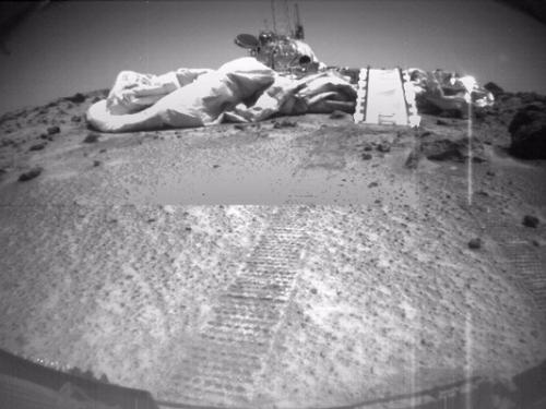 A view of the Mars Pathfinder lander, a set of paths and cushioning tarps designed to land the Sojourner rover on Mars, is passed by the Soujourner rover.