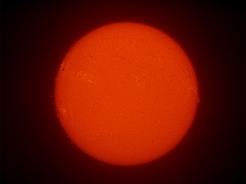 Disk view of the Sun with a large sunspot cluster visible on the left side of the Sun. 