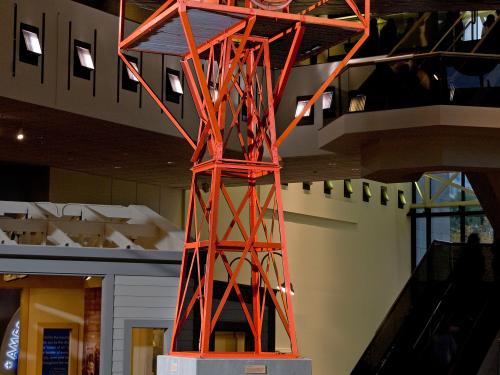 Orange, metal structure holding rotating light used for air travel. Structure is displayed in the Museum.