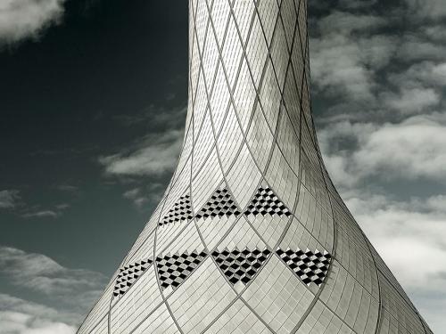 Partial view of white, conical shaped air control tower. The exterior features a tiled pattern throughout.