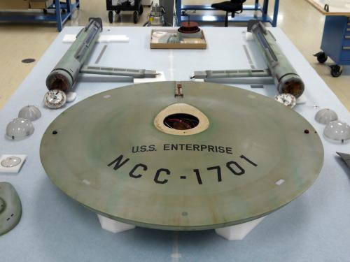 The major components of a gray-colored spaceship studio model are placed separately on a table. The saucer is closest in this perspective.