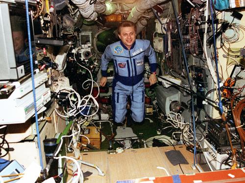 An astronaut floats inside the Mir Space Station, wires and tools float messily around him. 