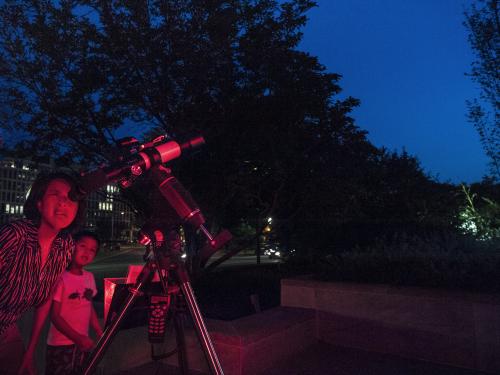 A mother and son use a telescope at night. 