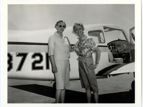 Black and white photo of Olive and Louise pose in front of airplane.