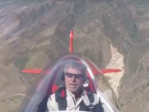 View of Sean Tucker in his red aircraft in flight. 