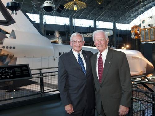 Two men pose in front of space shuttle. 