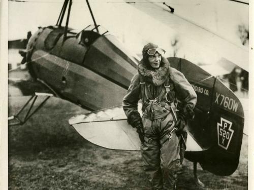 black and white photo of Amelia Earhart in front of an aircraft. 