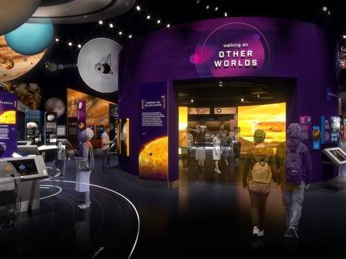 A rendering of a gallery showing planetary information. There are planets hanging from the ceiling and a purple wall in the center.