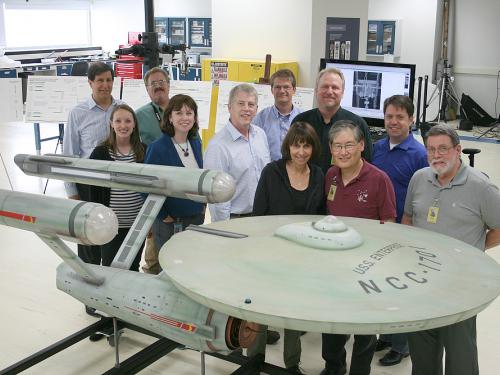A group of Museum employees in charge of handling a gray spaceship studio model from the Star Trek series stand behind the studio model.