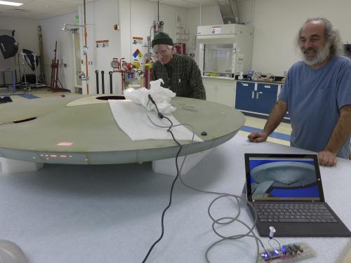 Two Museum specialists test lighting to match the original lighting as part of a gray spaceship studio model used in the Star Trek television series.