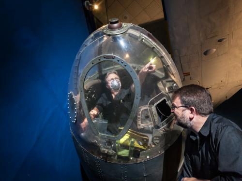 Two white male museum specialists work together to remove a partial fuselage of a historic World War II bomber aircraft from public display in the Museum.