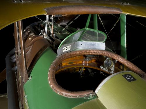 A close-up look at the interior of an airplane cockpit, which is painted green on the outside. The cockpit interior is made of polished wood, bounded by a strip of sewn leather around the rim.