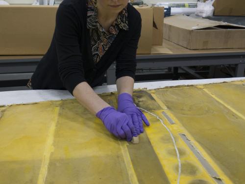Conservator with purple gloves works over yellow rudder fabric.