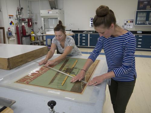 Two conservators working over an airplane print. 