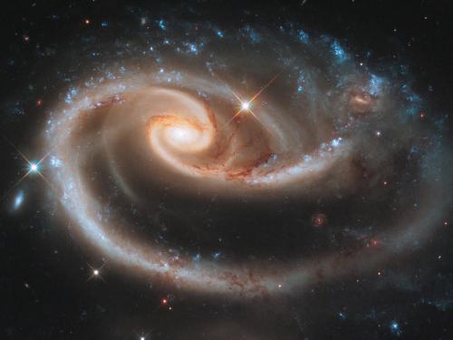 image taken from space telescope of a distant galaxy with swirling bright arms full of stars on a black backdrop of space