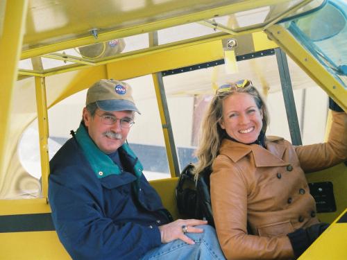 John and Heather Penney sitting in the cockpit of a yellow plane. 