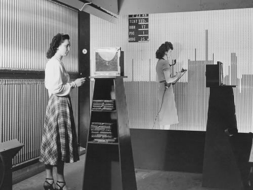 Two women stand at larger boards. 