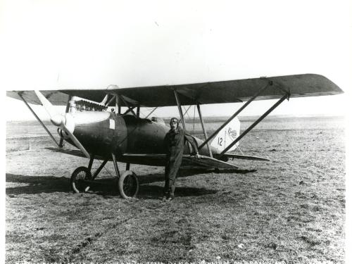 Black and white photograph of airplane with pilot in front.