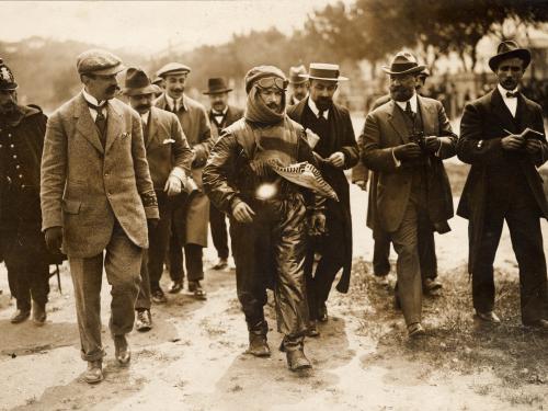 Black and white of Jules Vedrines wrapped in a leather flying suit and surrounded by others.