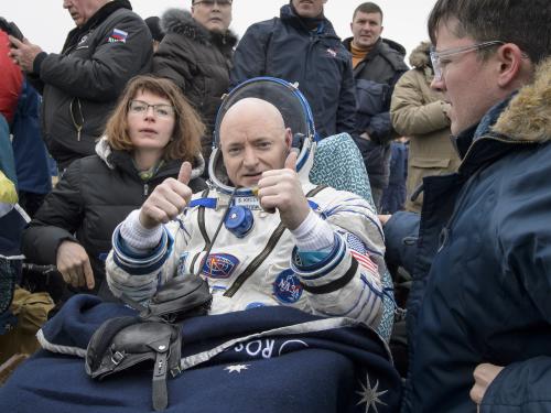 Kelly sits in his spacesuit while a crowd surrounds him. 