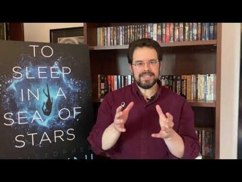 An author sits in front of is bookcase while discussing science fiction.