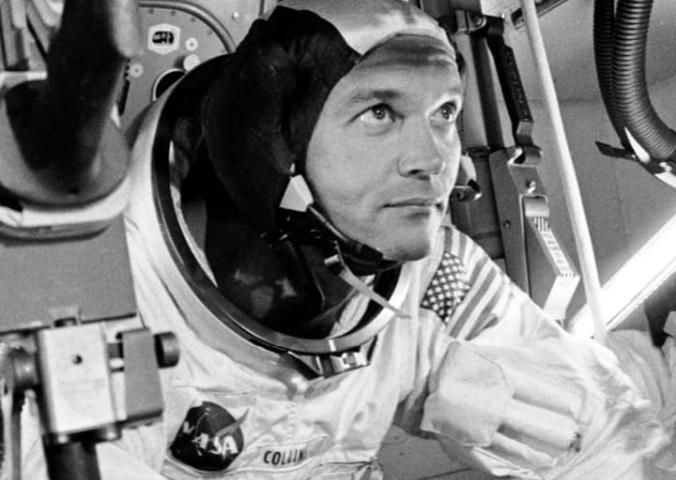 A man, Michael Collins, in a space suit looking out. 