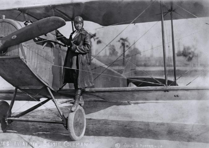 A woman stands on the wing of an airplane.