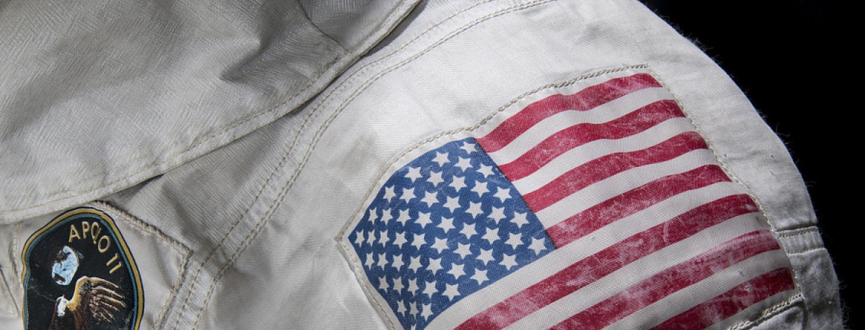 A close up of the should of Neil Armstronng's spacesuit. An American flag patch and the mission patch are visible. 