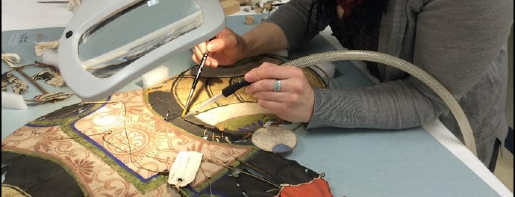 A museum conservator leans over a kite using tools to work on it. 