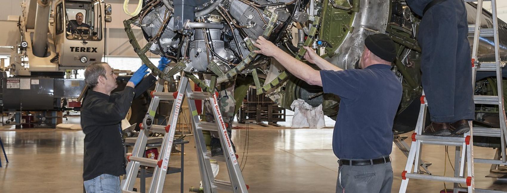 Three men guide an engine into position for restoration work.