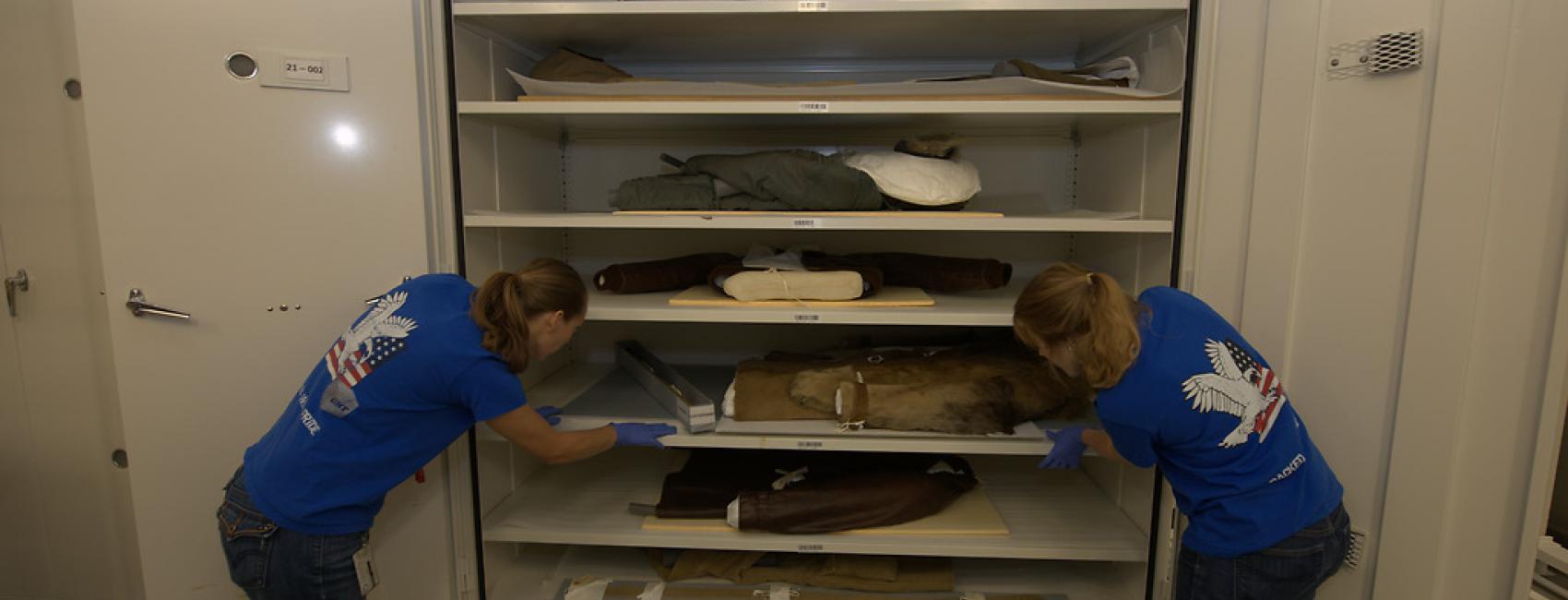 Two women look into a cabinet with artifacts.