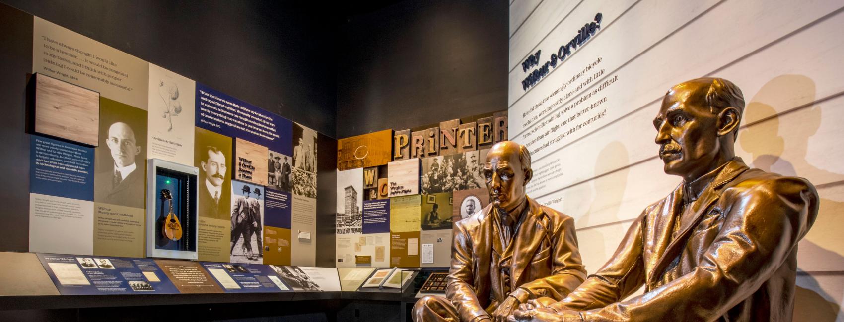 Two bronze statues sitting on steps at the entrance of a museum exhibit. 