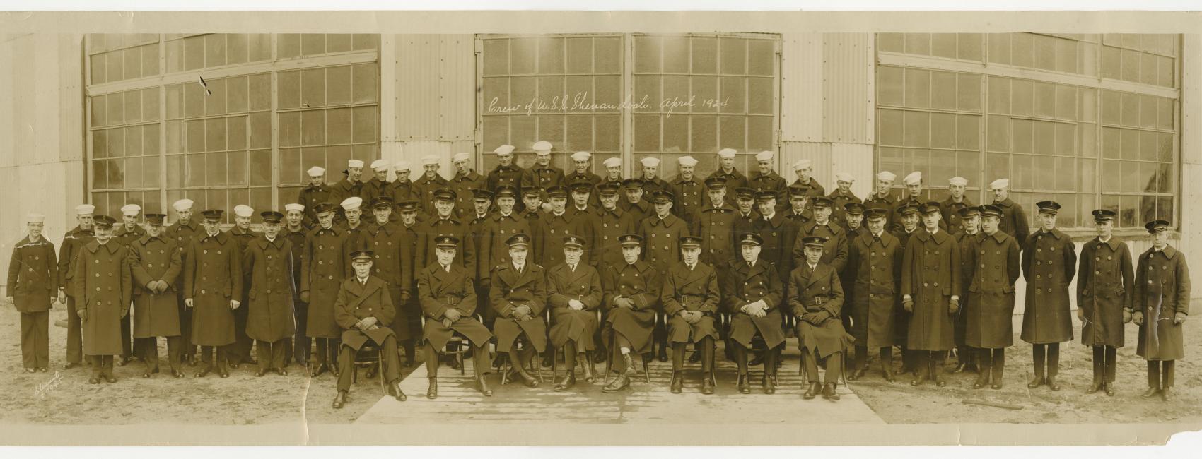  A partial view of a photograph of the entire crew of the USS Shenandoah in April 1924. A row of men sit posed in front of the camera with two rows of men standing behind them.