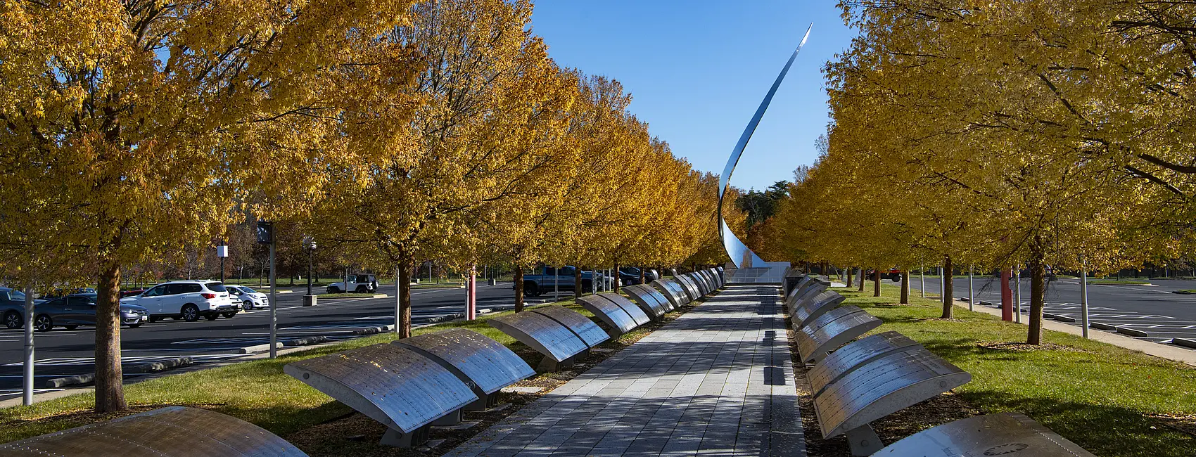 The Wall of Honor, plaques with different names lining a walkway, with a sculpture at the end in the daylight. 