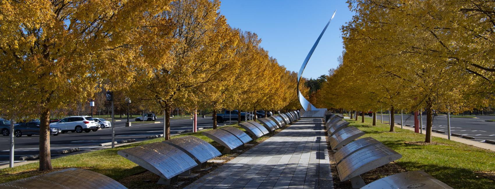 The Wall of Honor, plaques with different names lining a walkway, with a sculpture at the end in the daylight. 