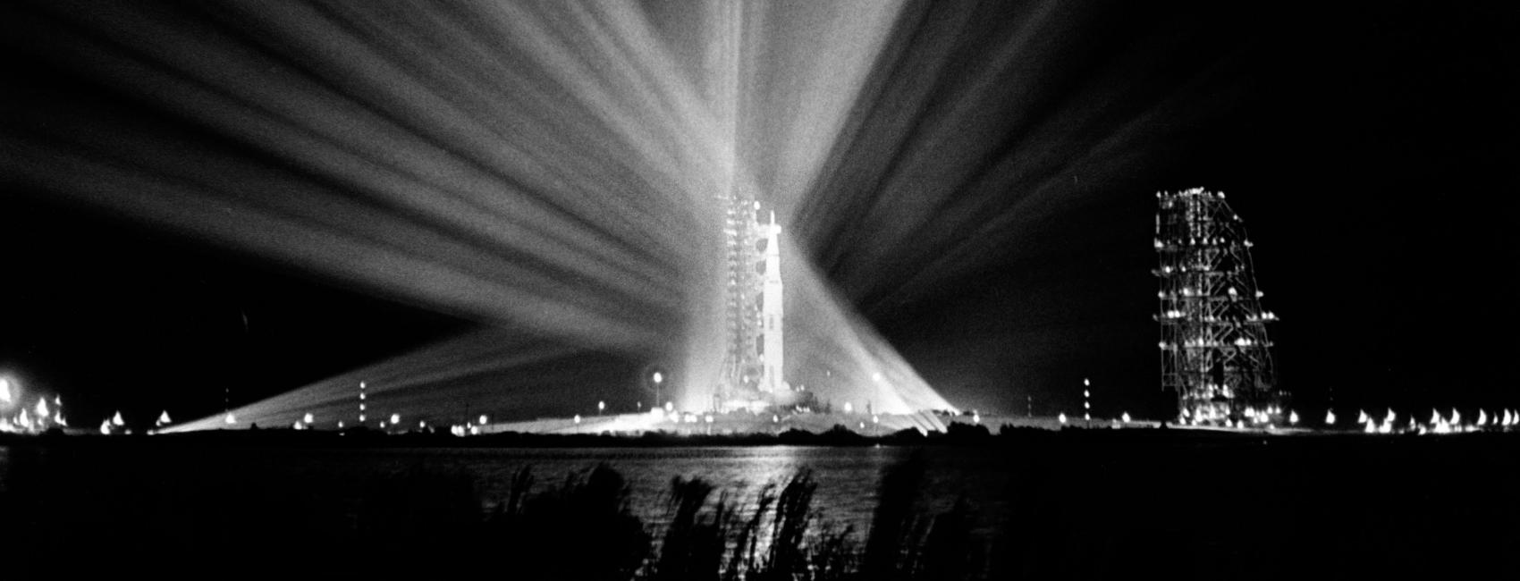 A black and white photograph of a rocket, illuminated by spotlights. 