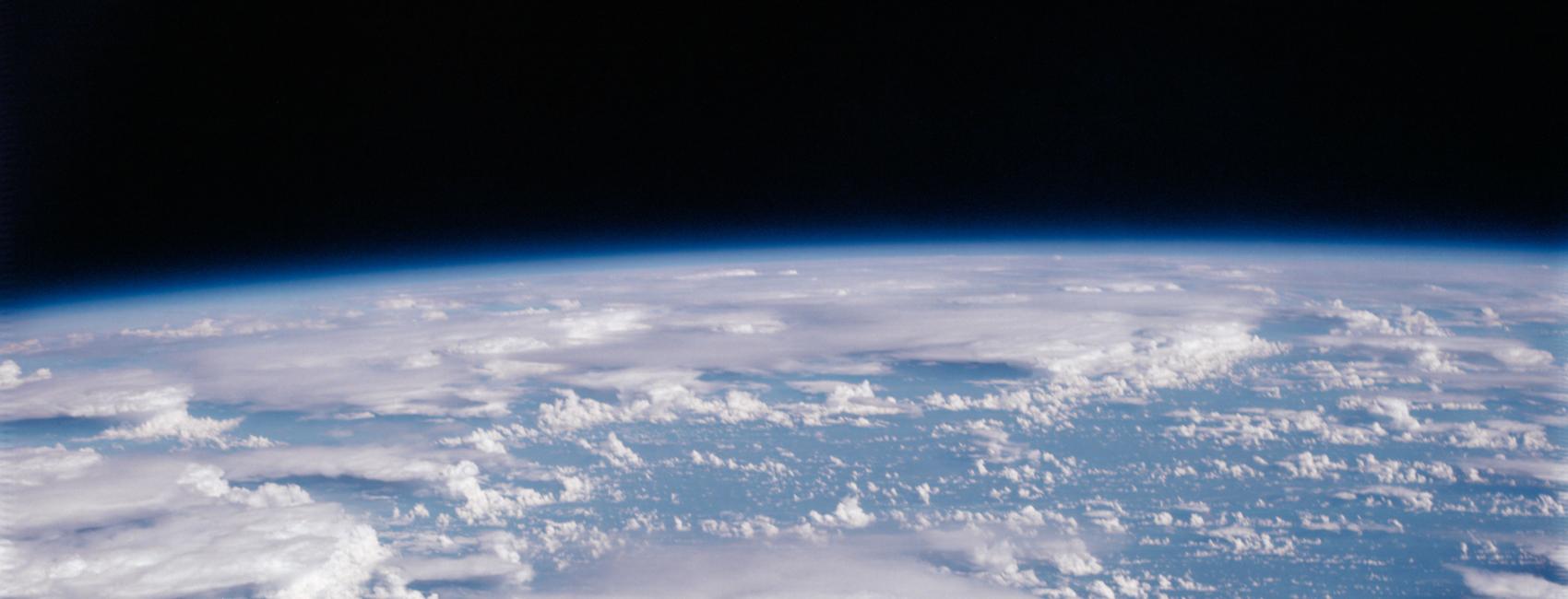 The blue sphere of the Earth, topped with swirling clouds, peeks out over a dark background. 