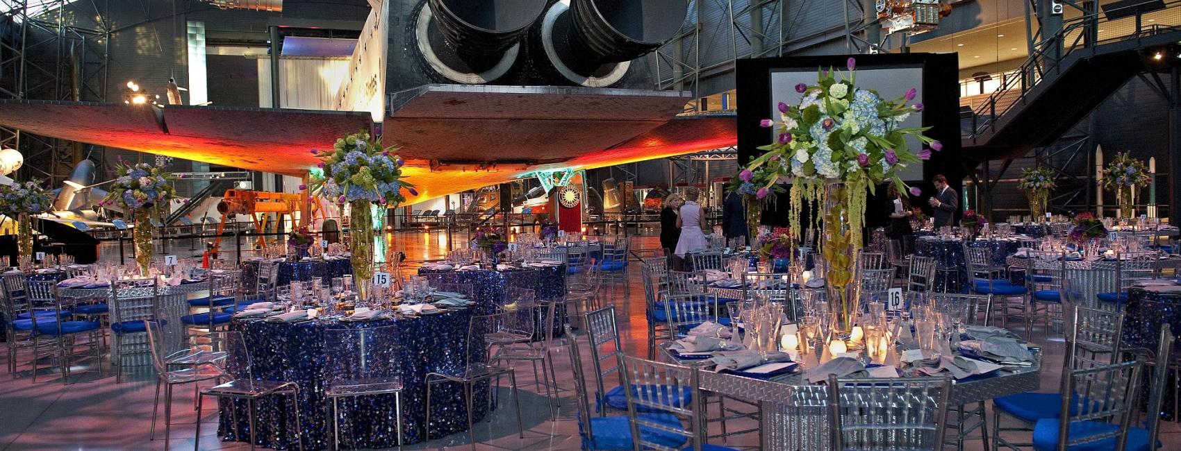 Tables with elaborate centerpieces are set up on the museum floor, in the rear of the Space Shuttle Discovery.