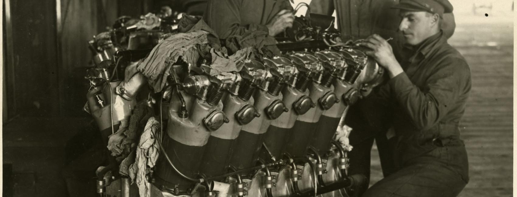 Three people examine a twelve-cylinder engine used for long-travel flight.