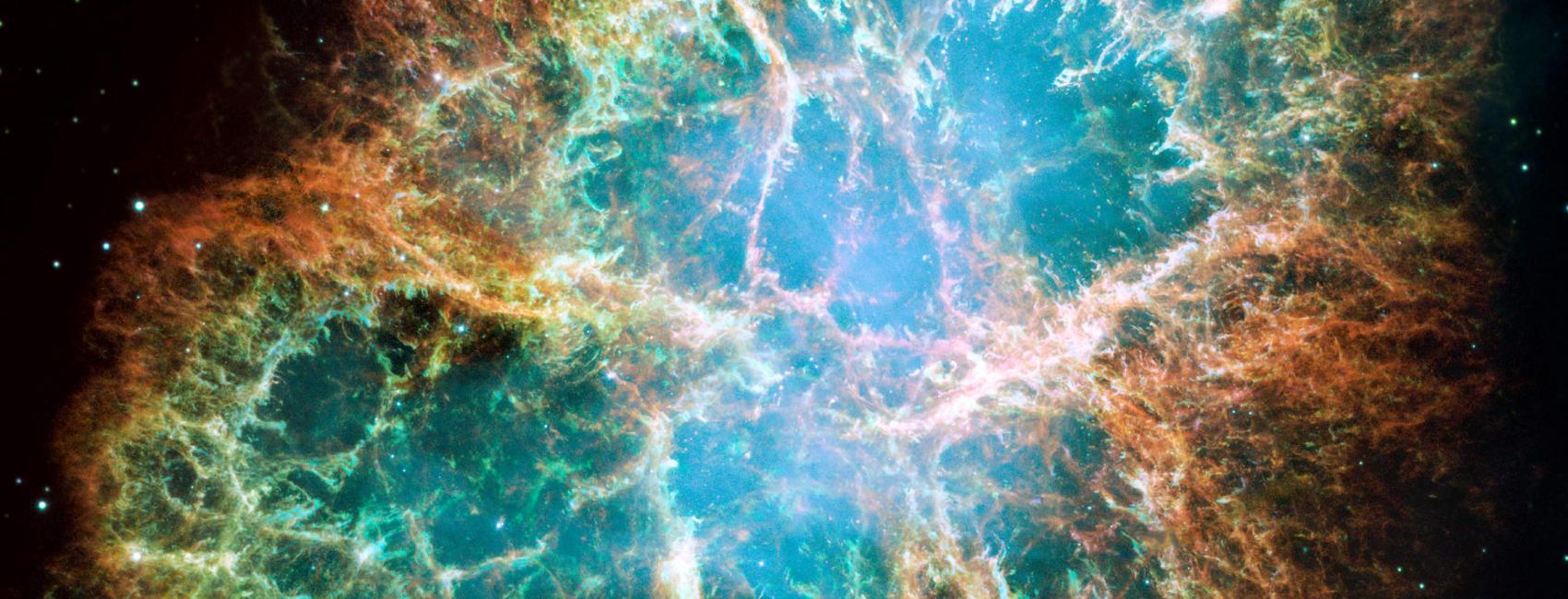 An image taken by a space telescope and colorized by scientists and artists, this gives us a picture of the cosmos. The edges are black with white glowing dots that appear as stars. In the center is the crab nebula, an organic circular shape that opens like a wound or a rip in the the black starry field. There are spindly formations that stretch towards the center of the opening, layers and layers deep, like vines. The opening is mostly shades of blue and green, with some orange around the edge.